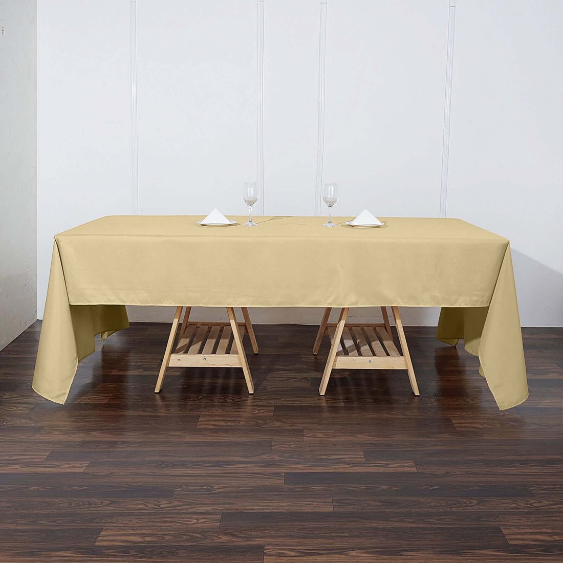 Beige tablecloth on a wooden table with glasses and napkins.