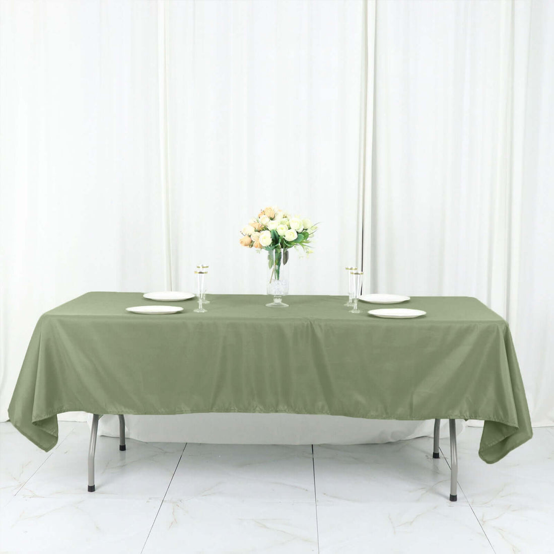 Olive green tablecloth draped over a table with plates and a flower centerpiece.