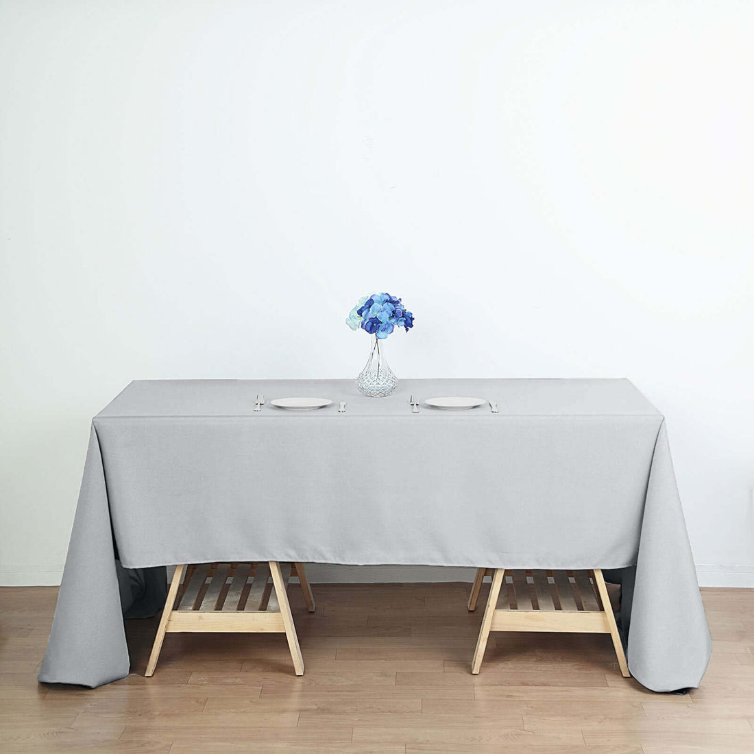 Gray tablecloth draped over a wooden table with a vase of blue flowers.