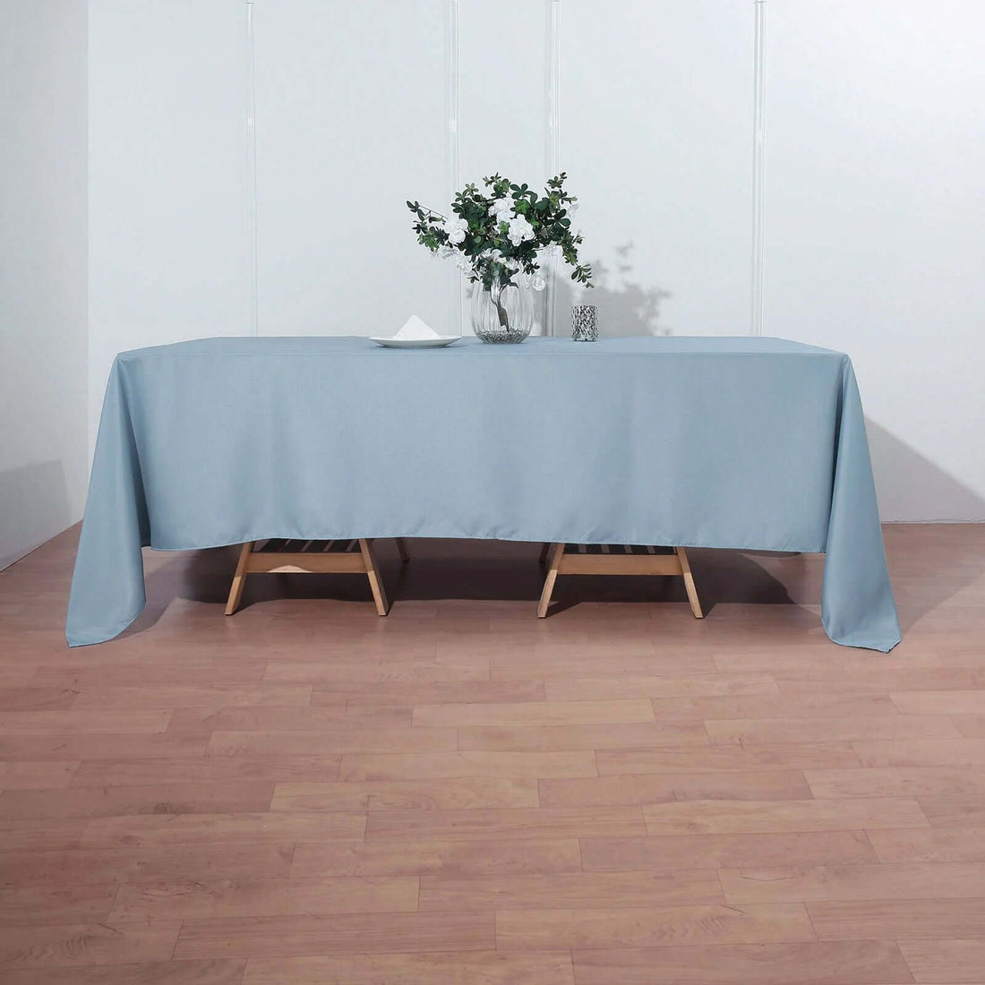 Light blue tablecloth draping over a wooden table with a vase of flowers