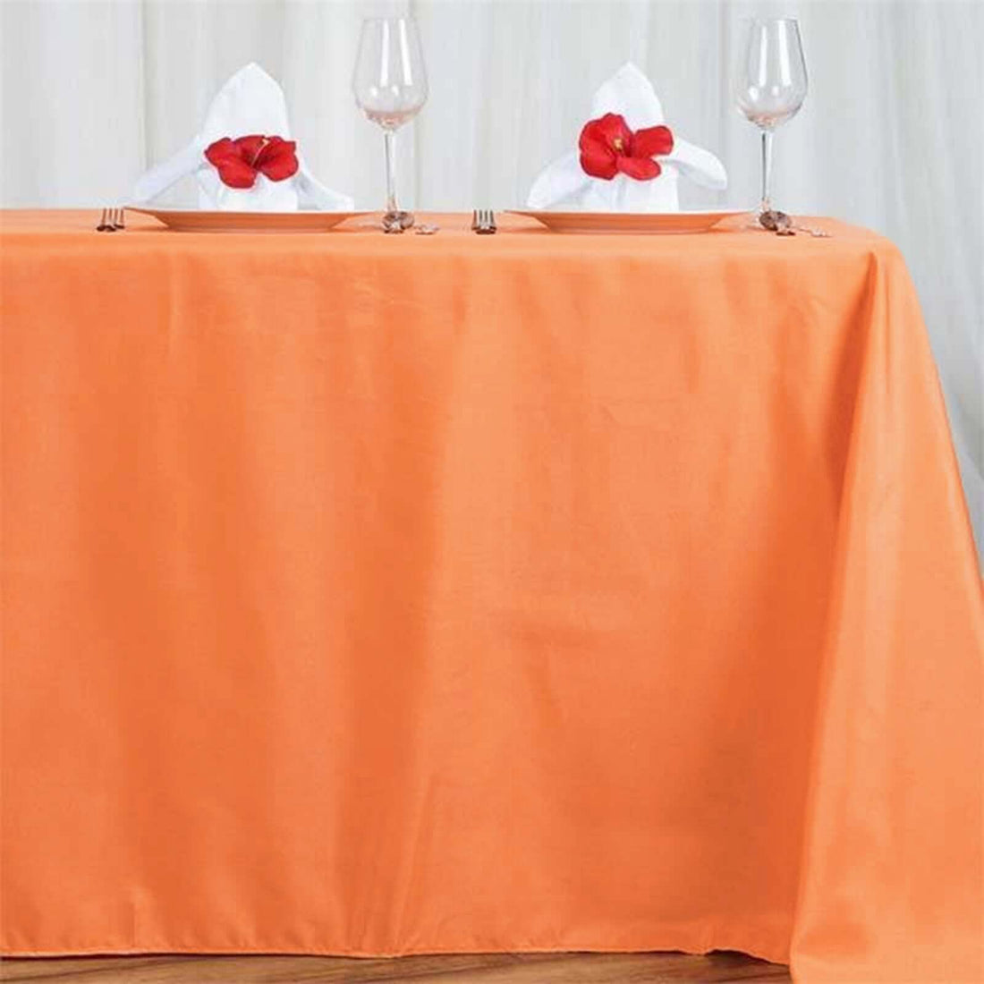 Orange tablecloth set with glassware and decorated napkins.