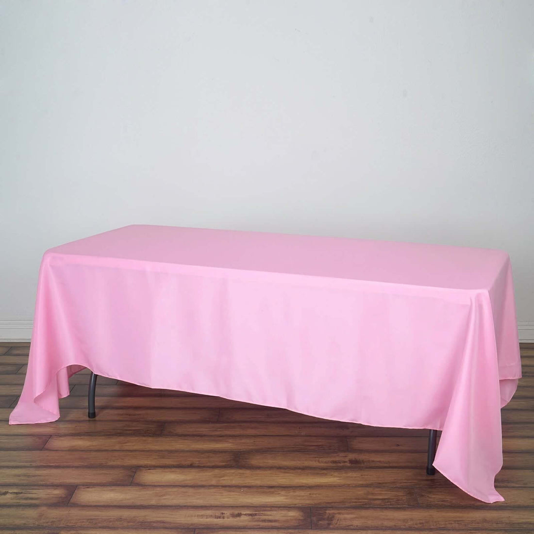 Pink tablecloth draped over a table on a wooden floor.