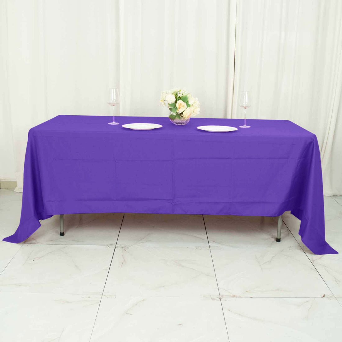 Purple tablecloth draped over a table with plates and a flower vase.