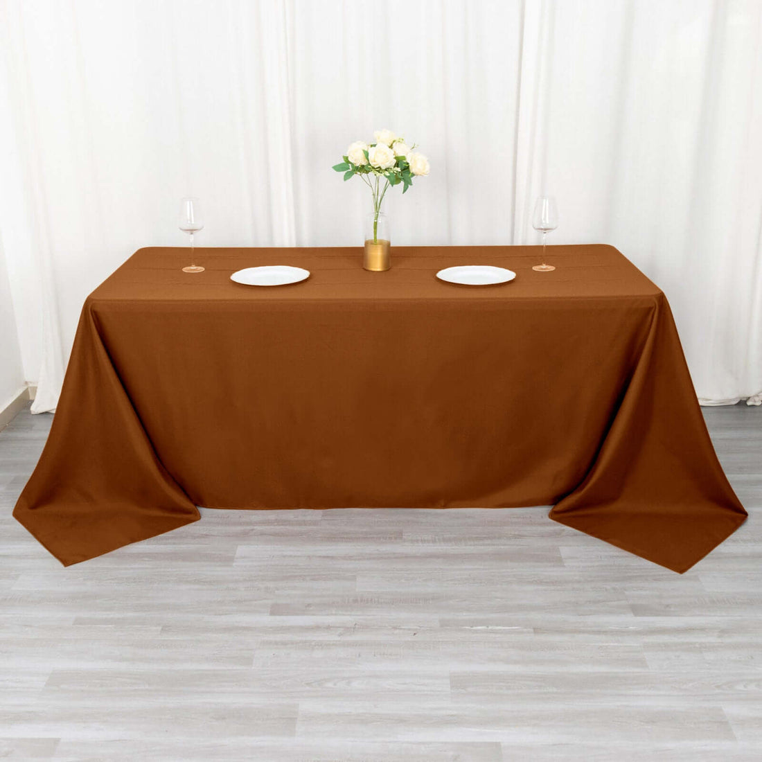 Brown tablecloth draped over a table set for dinner with plates and flowers.