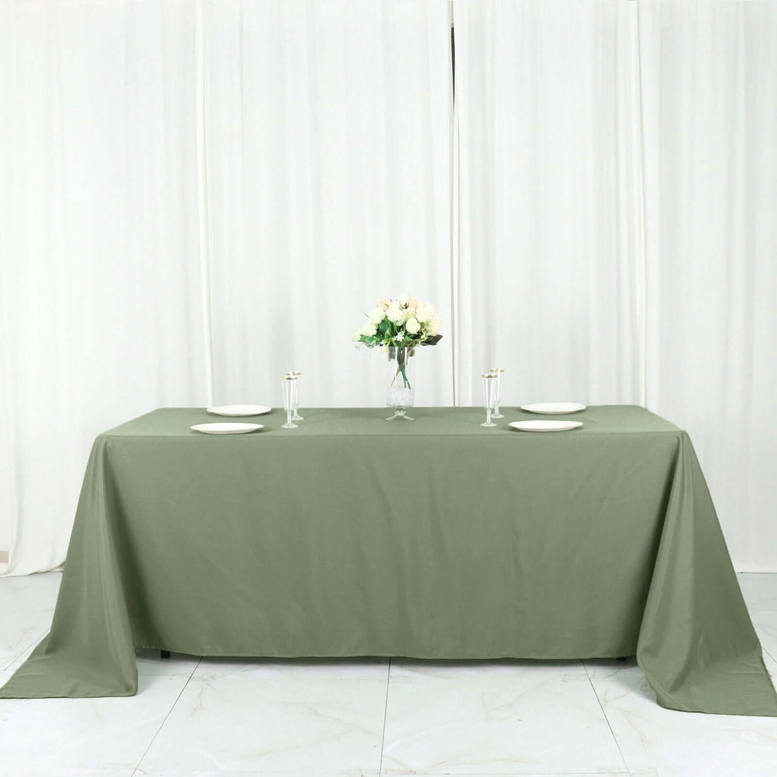 Olive green tablecloth draped over a table with plates and a floral centerpiece.