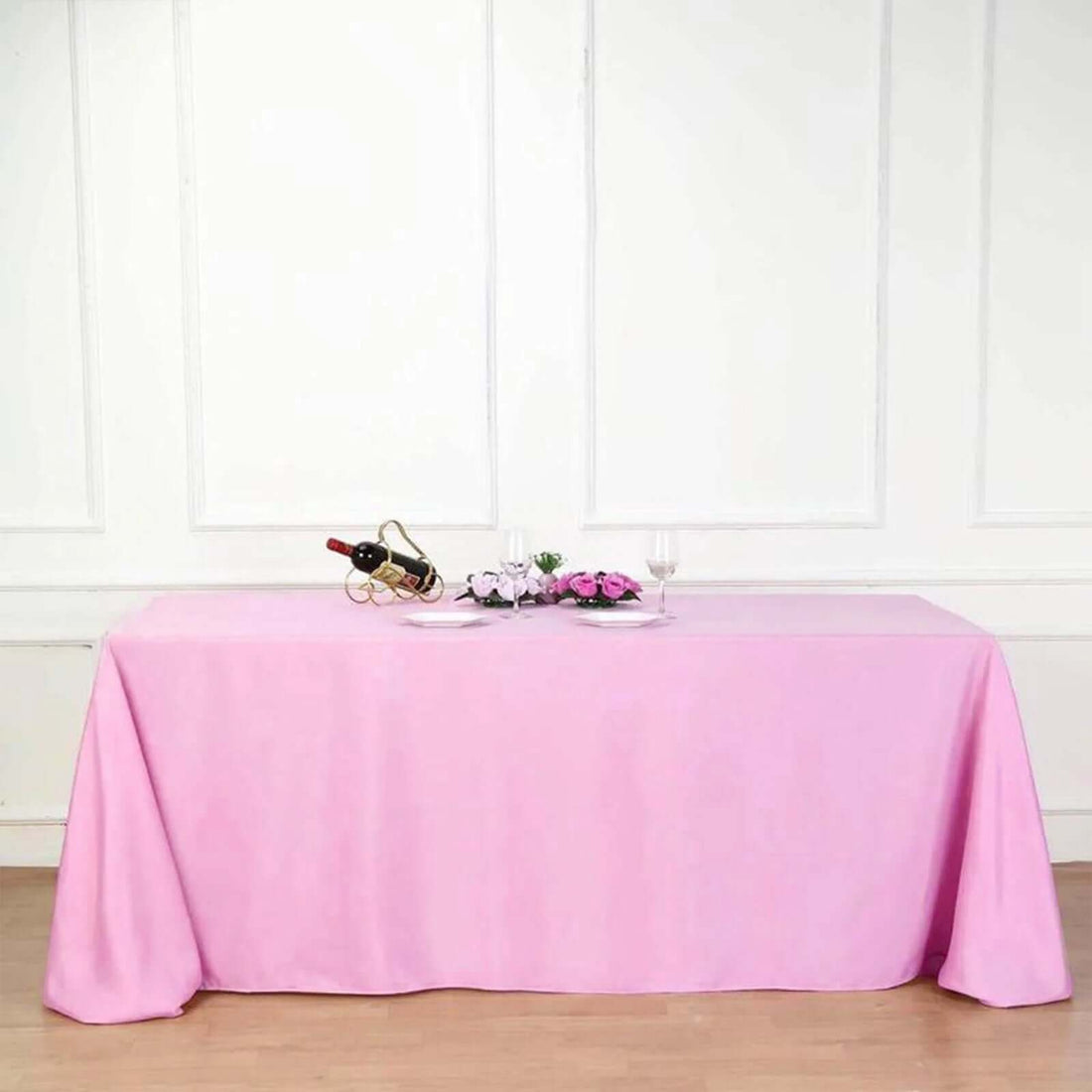 Pink tablecloth draped over a table with wine glasses and flowers.
