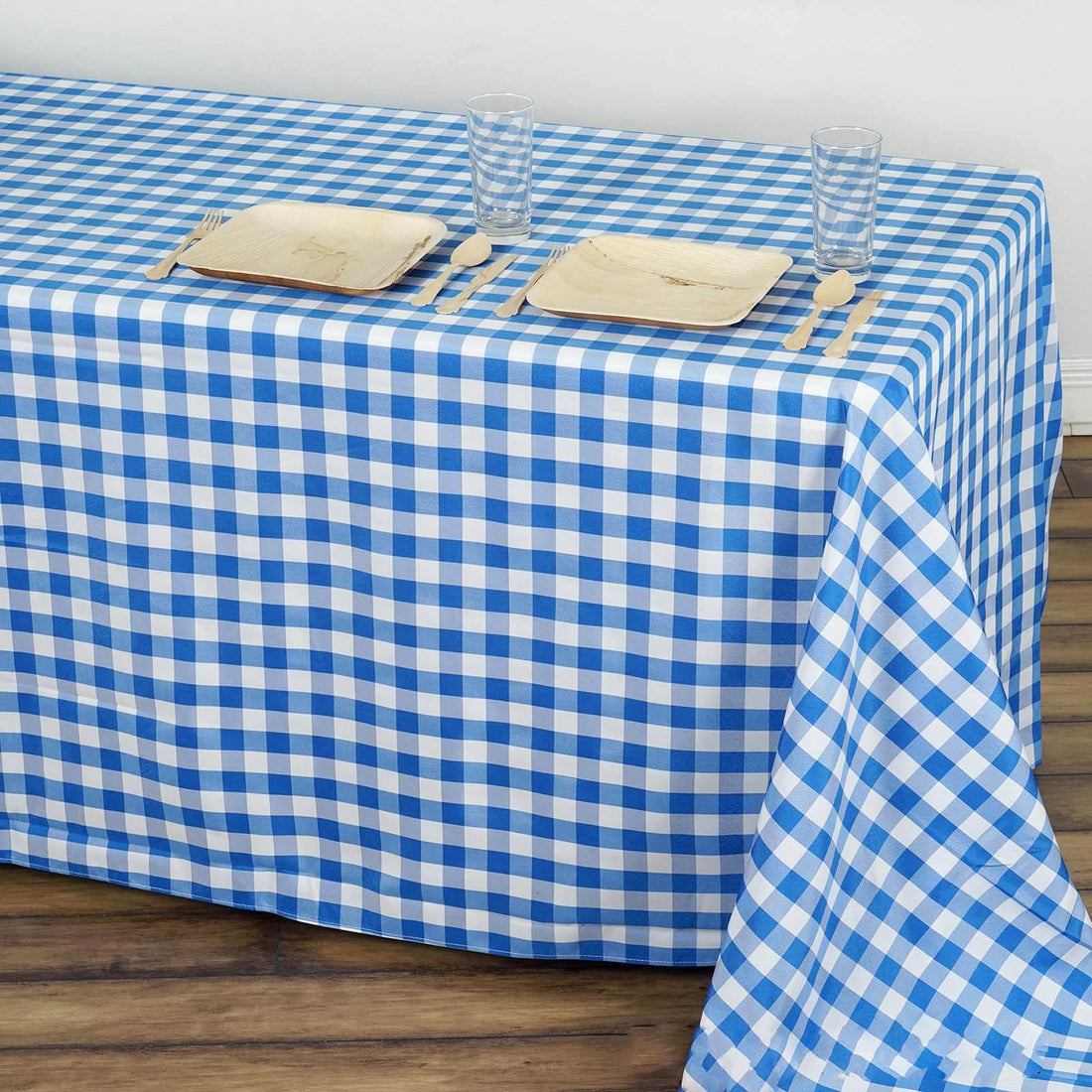 Blue and white checkered tablecloth on a wooden table with plates and glasses.