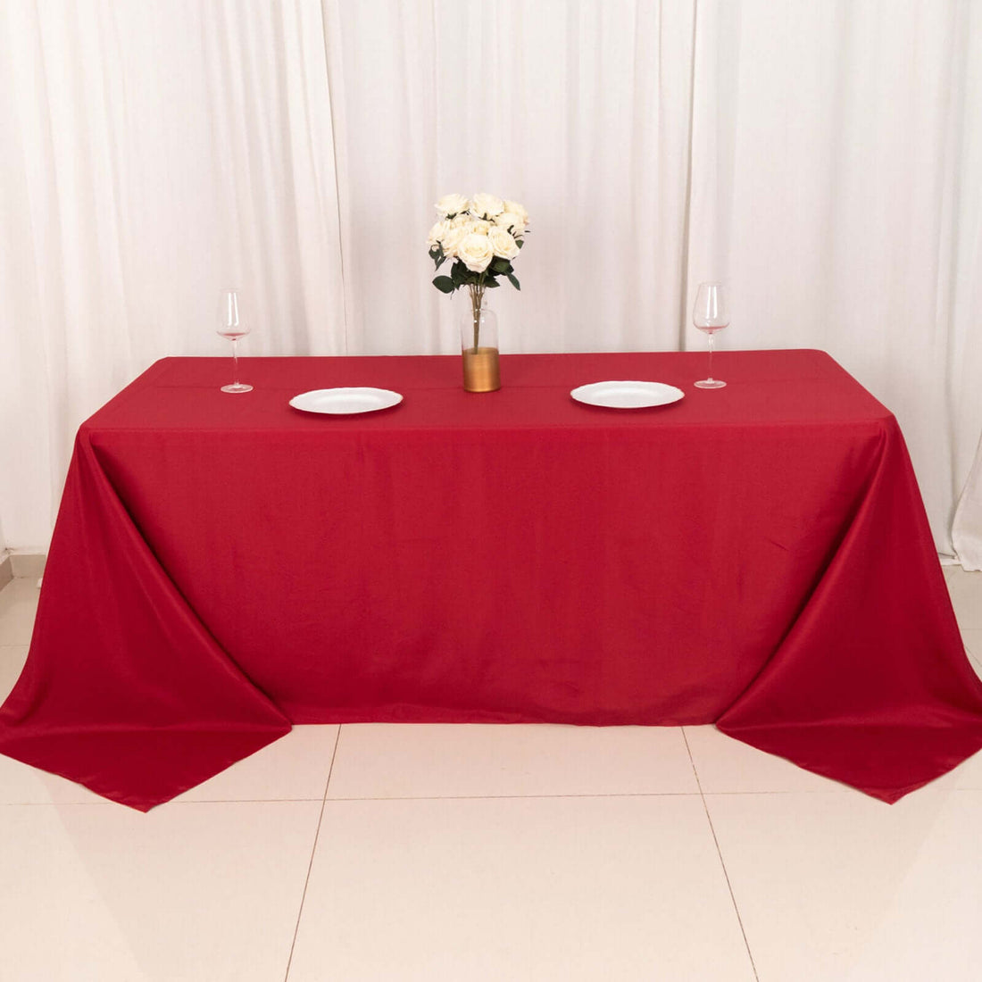 Red tablecloth draped over a table set for dinner with flowers and plates.