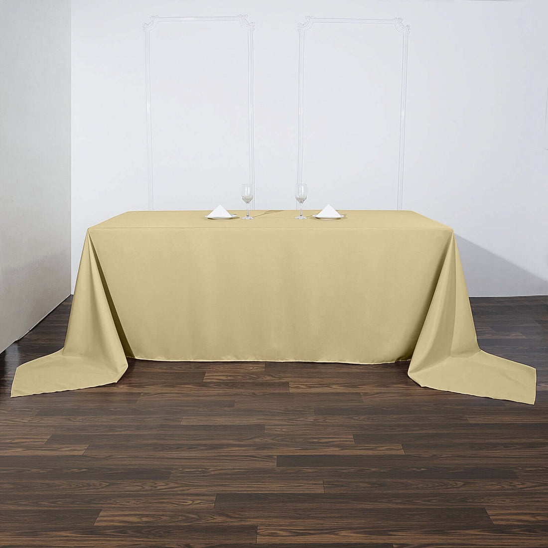 Beige tablecloth draped over a table with glasses and napkins on a wooden floor.