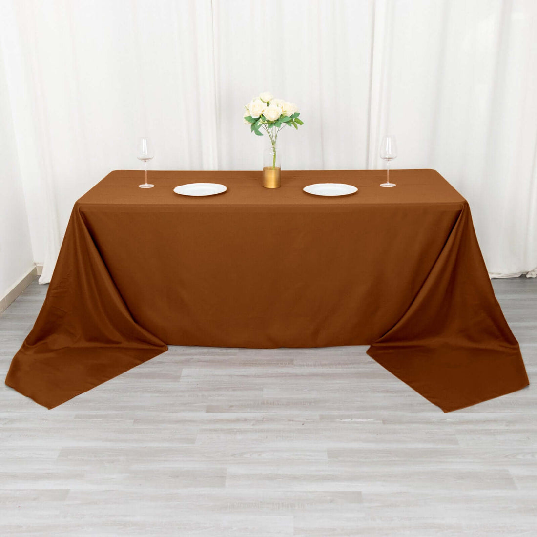 Brown tablecloth draped over a table set for dining with plates and glasses.