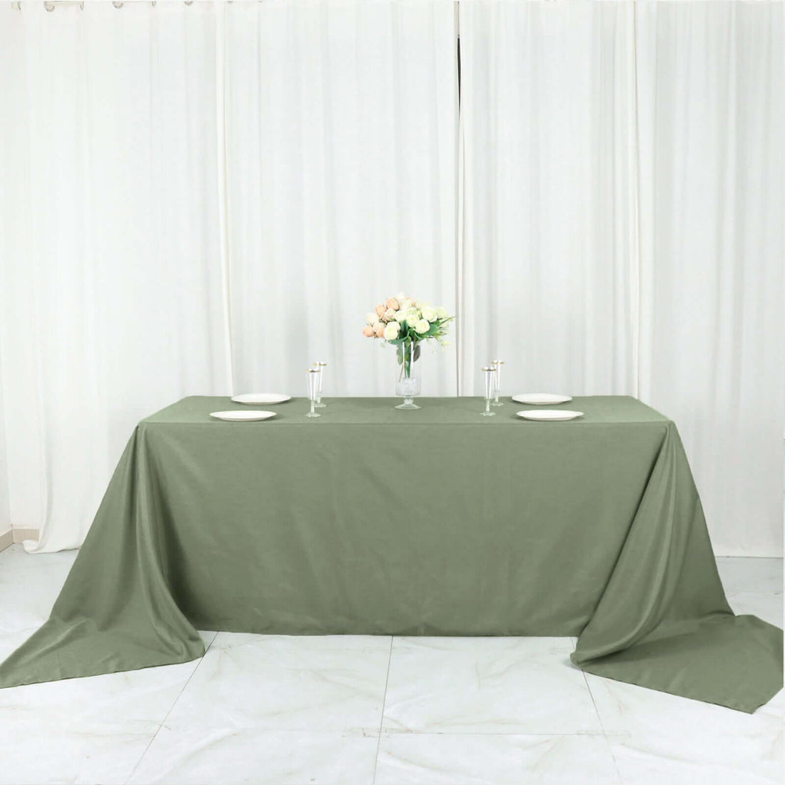 Olive green tablecloth draped over a table with plates and a vase of flowers.