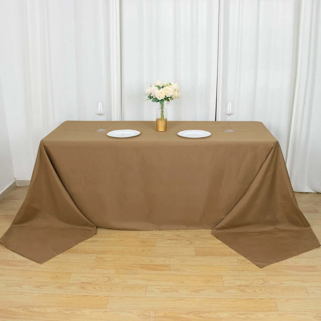 Brown tablecloth draping over a table set for dining with plates and flowers.