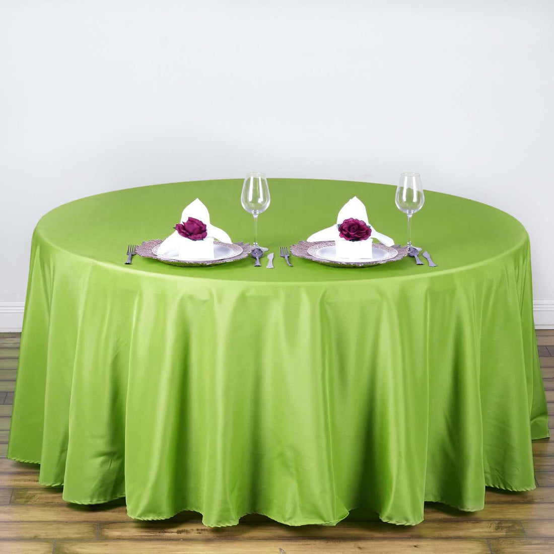 Green round tablecloth set for dining with elegant table setting.