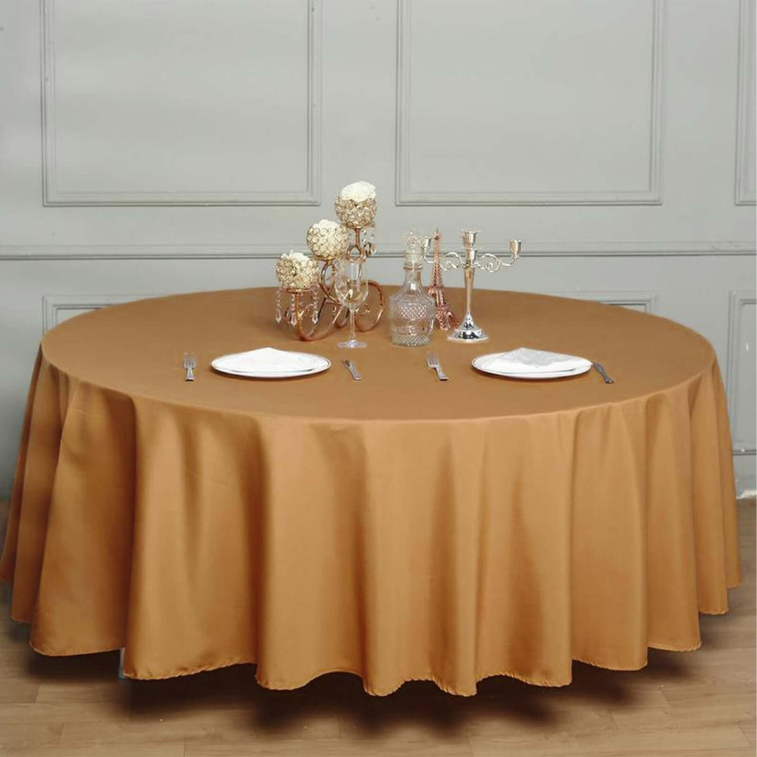 Round brown tablecloth on a dining table set with plates and decorative candles.