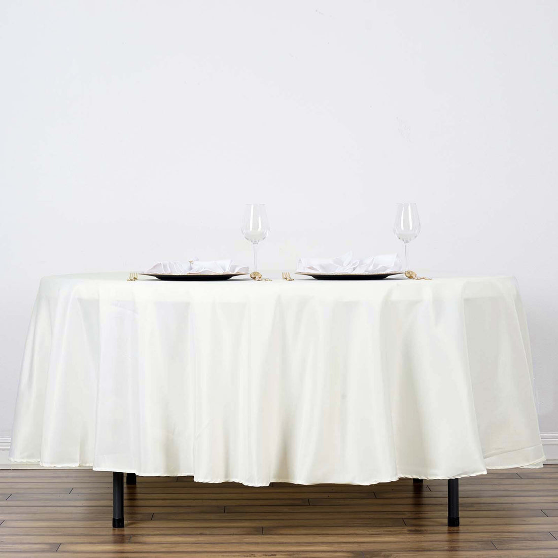 Elegant round table set with white cloth, plates, and glasses.
