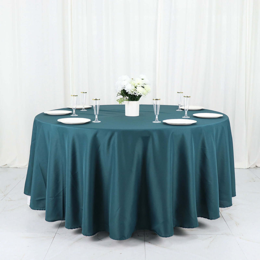 Round teal tablecloth draped over a table set with dishes and a floral centerpiece.