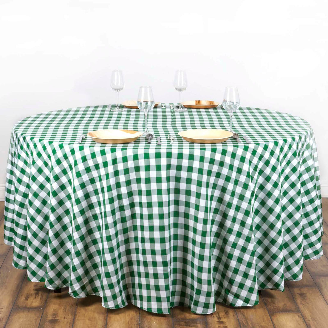 Green and white checkered tablecloth on a round table with plates and glasses.
