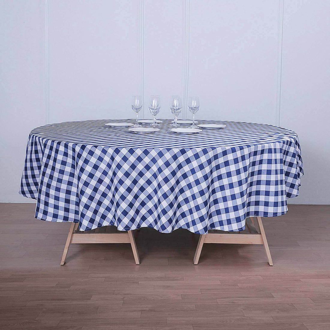 Round blue and white checked tablecloth on a wooden table with glasses.