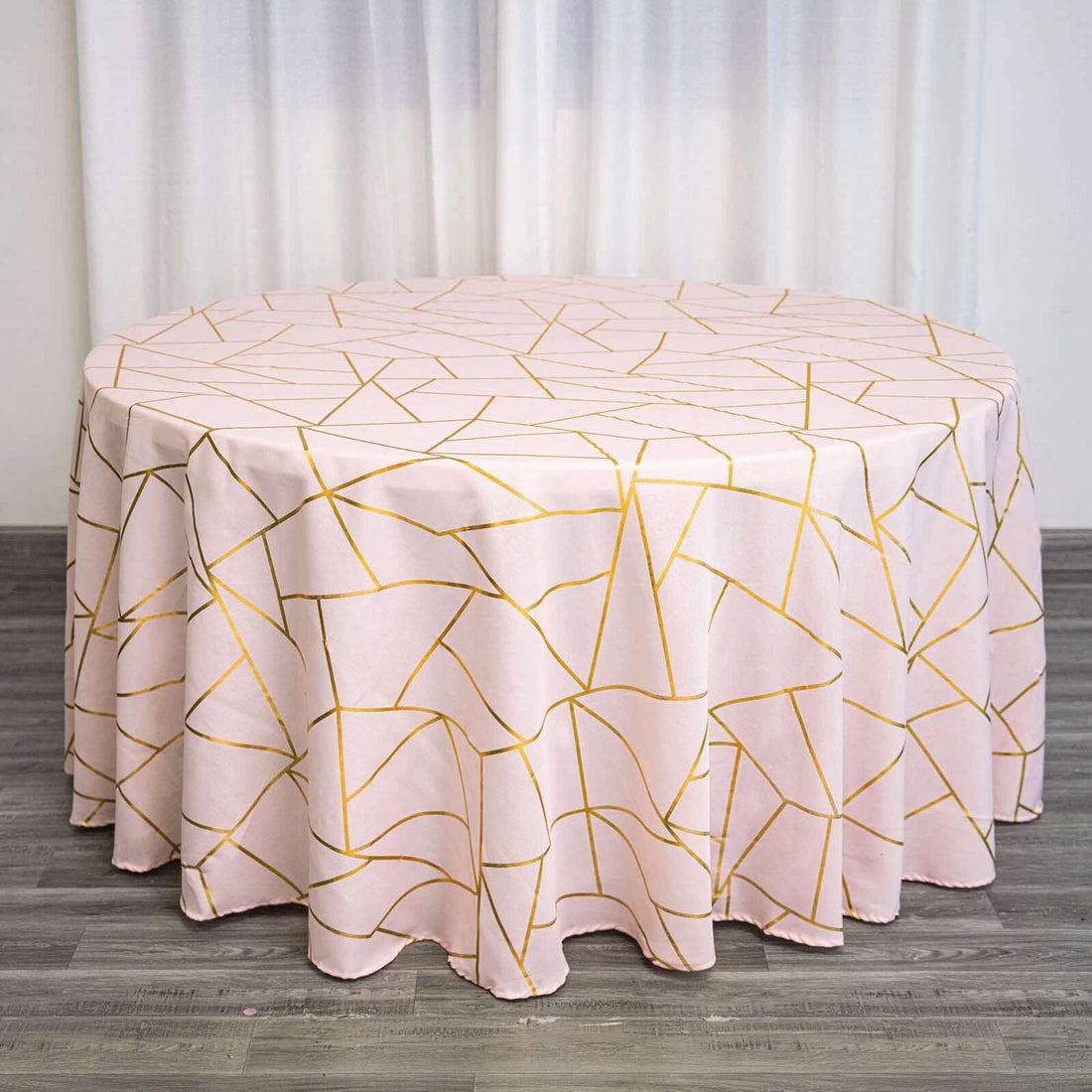 Round pink tablecloth with geometric gold pattern on a wooden surface.