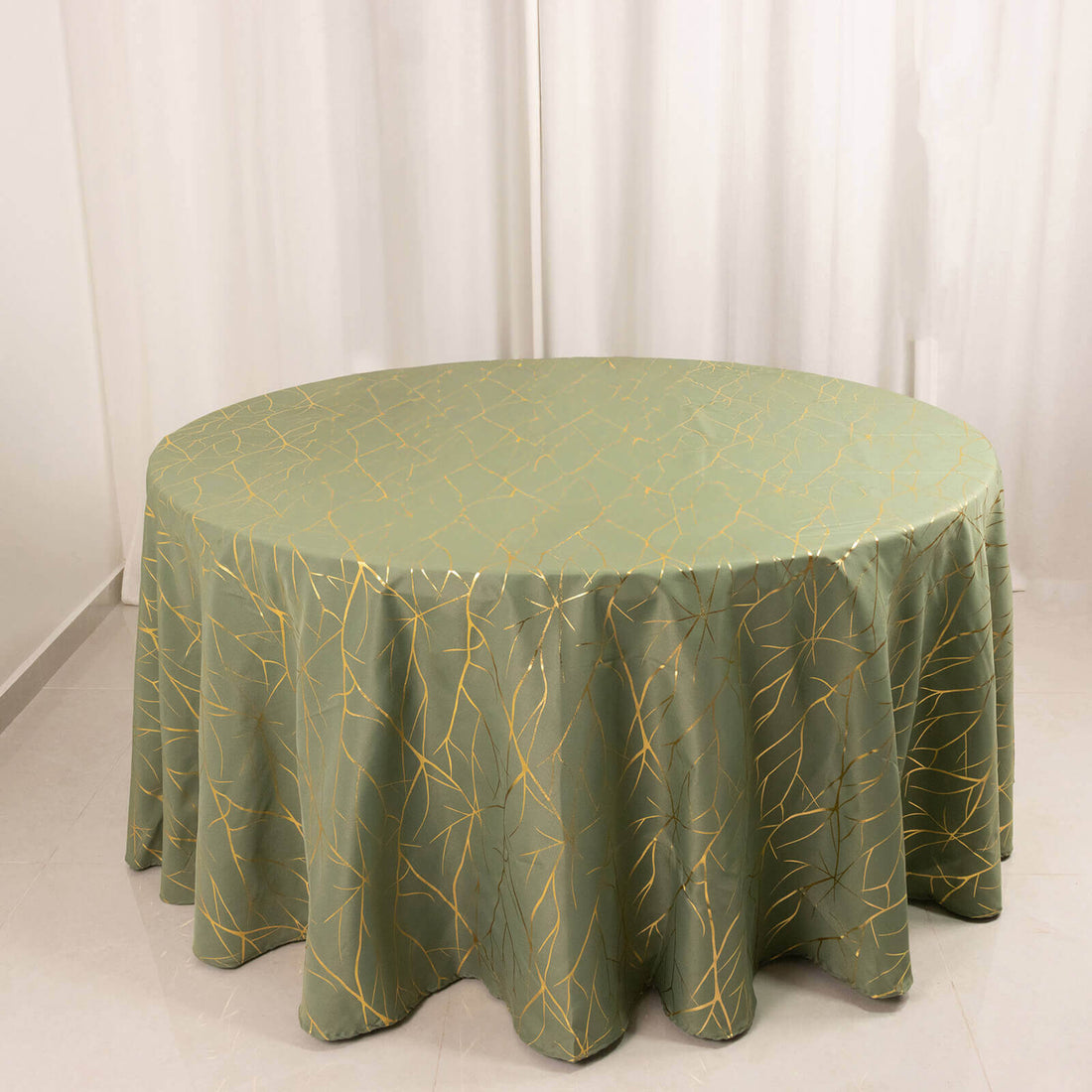 Round green tablecloth with golden leaf pattern on plain backdrop.
