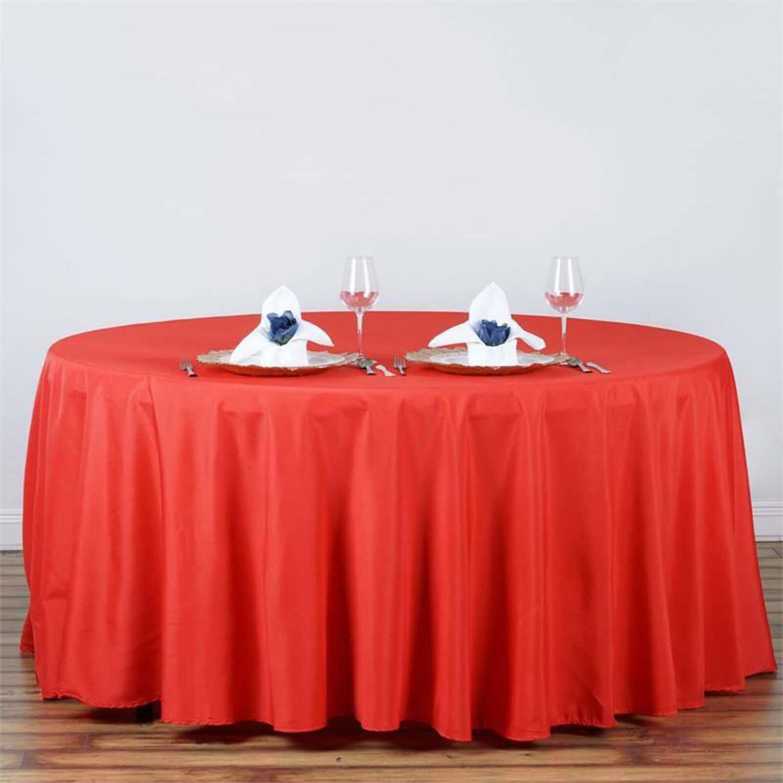 Red round tablecloth with dining setup featuring plates, napkins, and wine glasses.