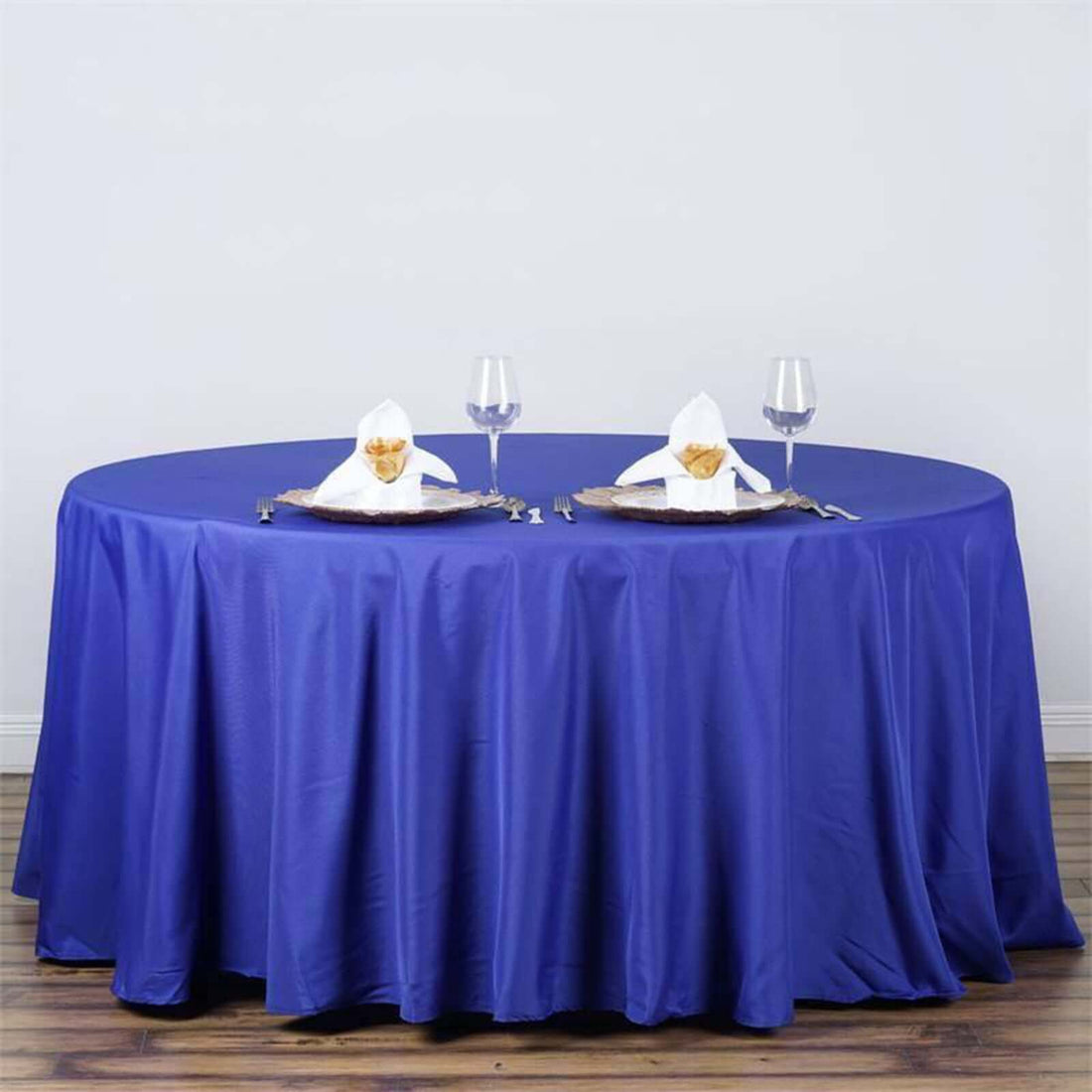 Round blue tablecloth on a table set for dining with glasses and napkin decor.