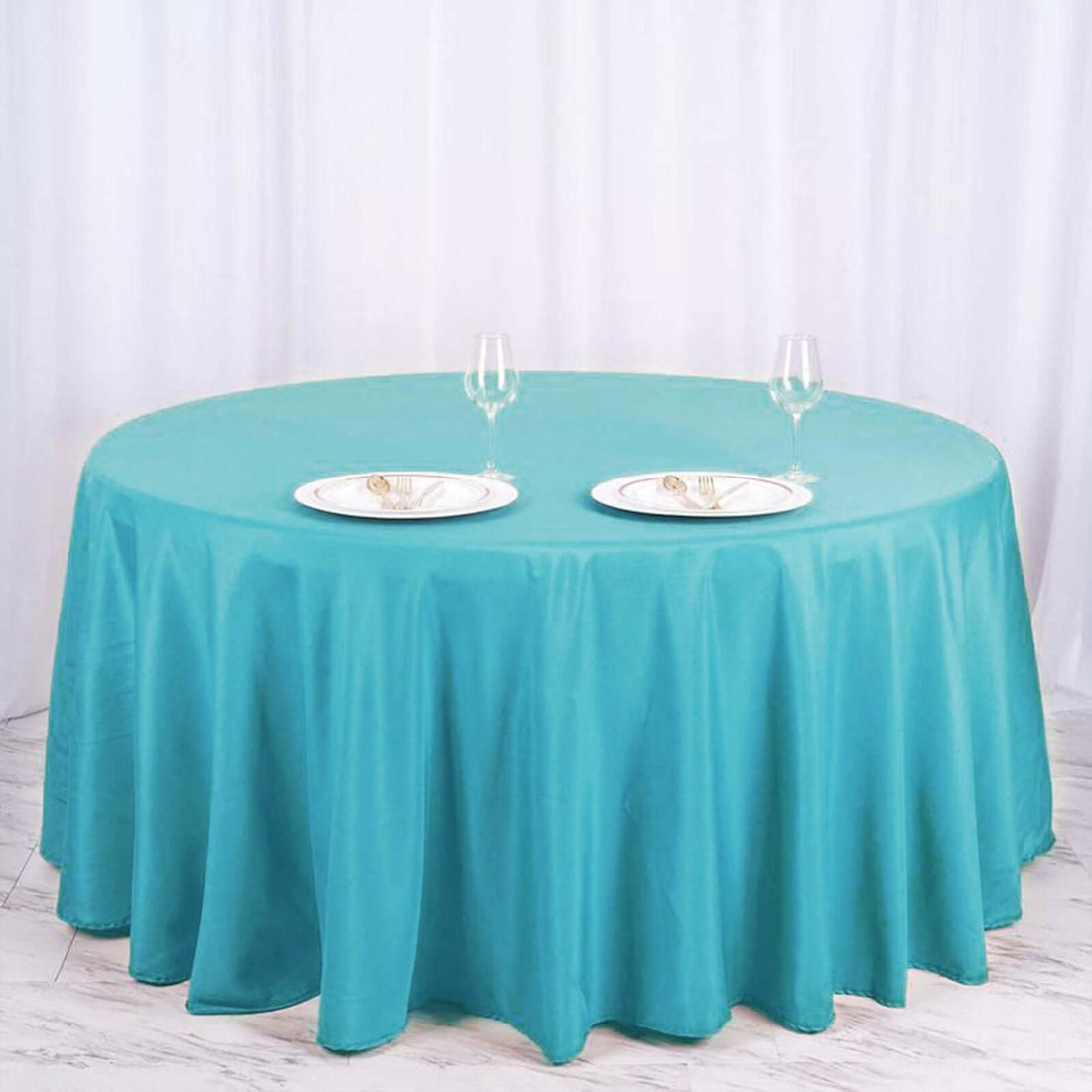 Round turquoise tablecloth with plates and glasses set on a white table.