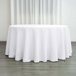 Round white tablecloth on a wooden floor with curtains in the background.
