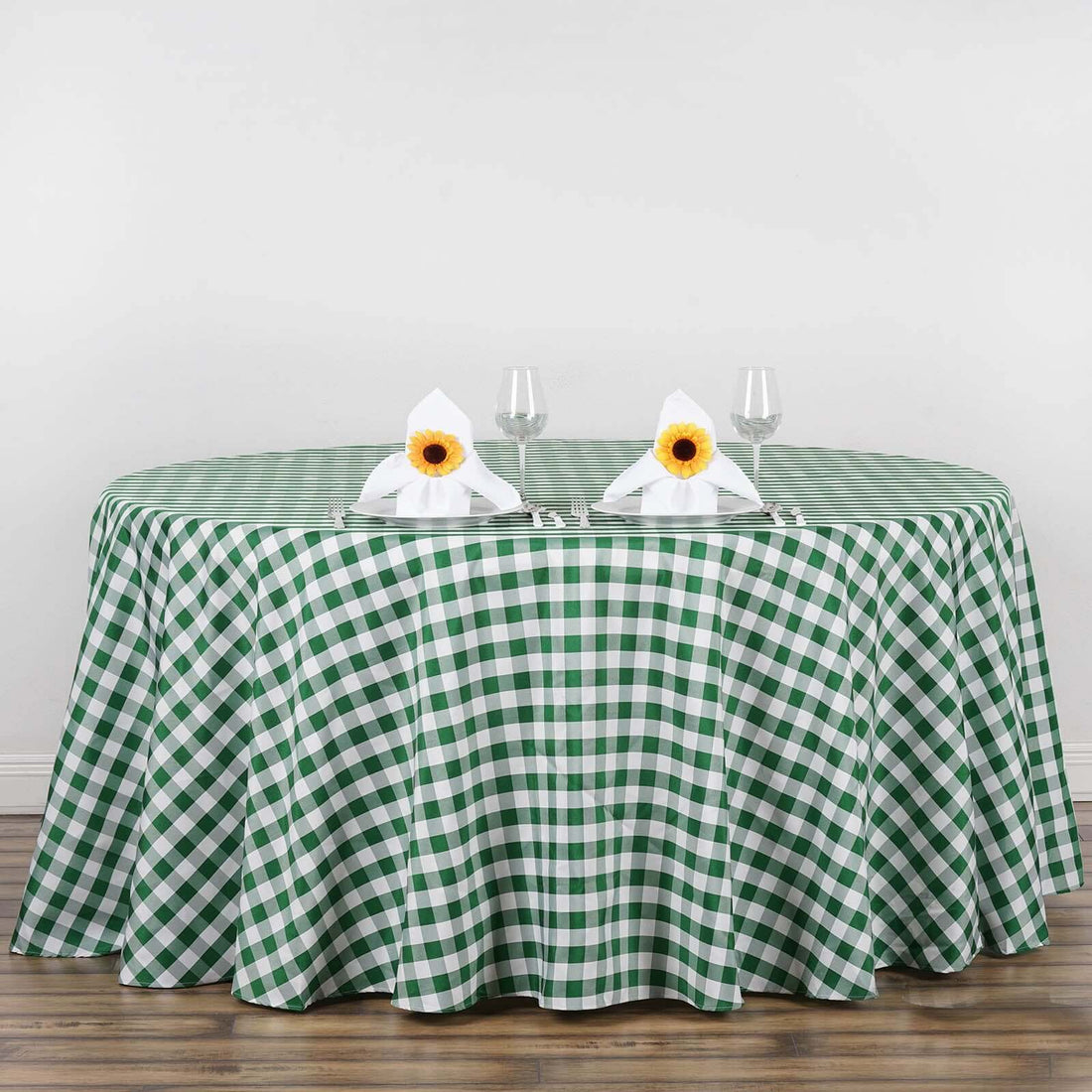 Green and white checkered tablecloth with napkins and glasses on a round table.