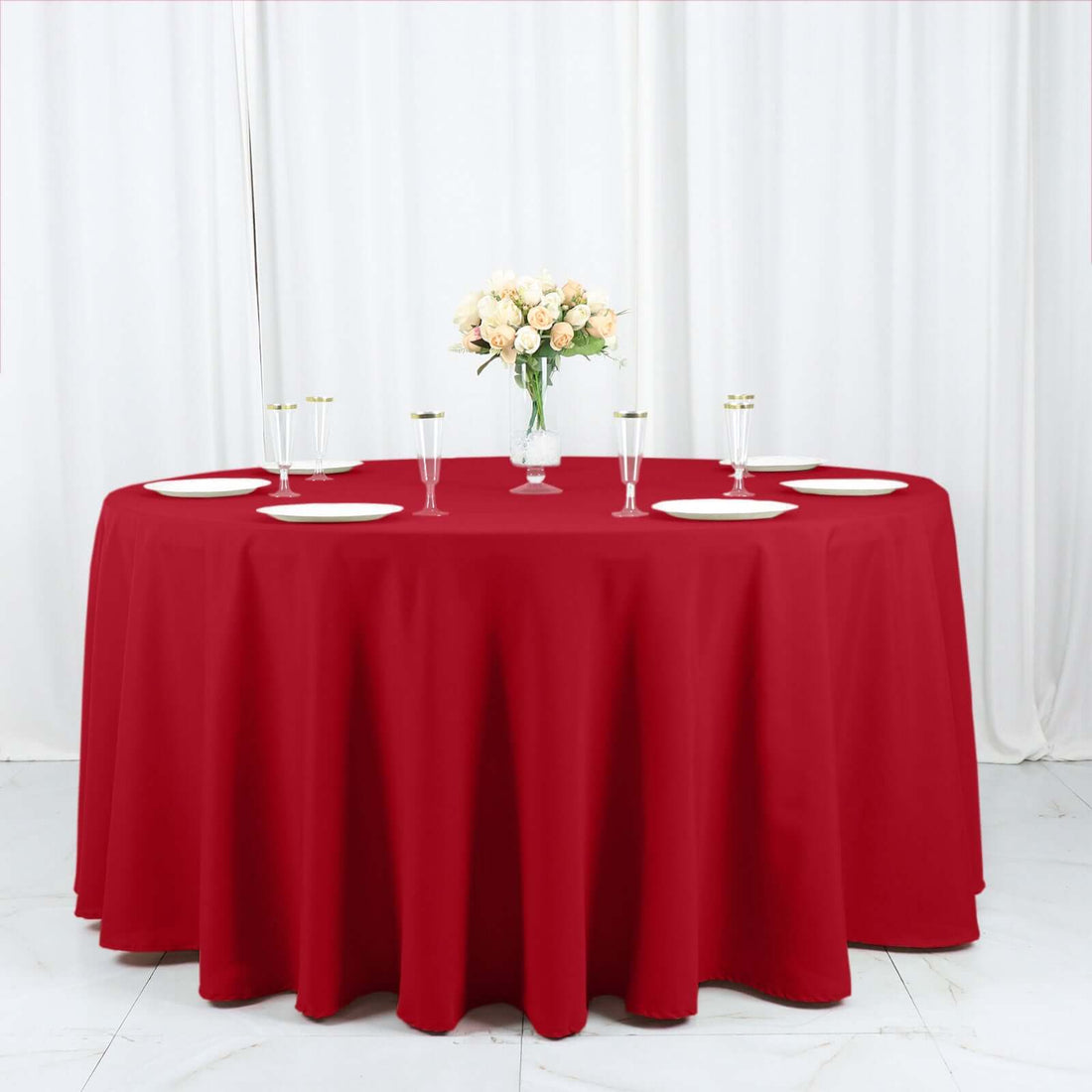 Red tablecloth draped over a round table set for dining with plates and glasses.