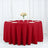 Red tablecloth draped over a round table set for dining with plates and glasses.