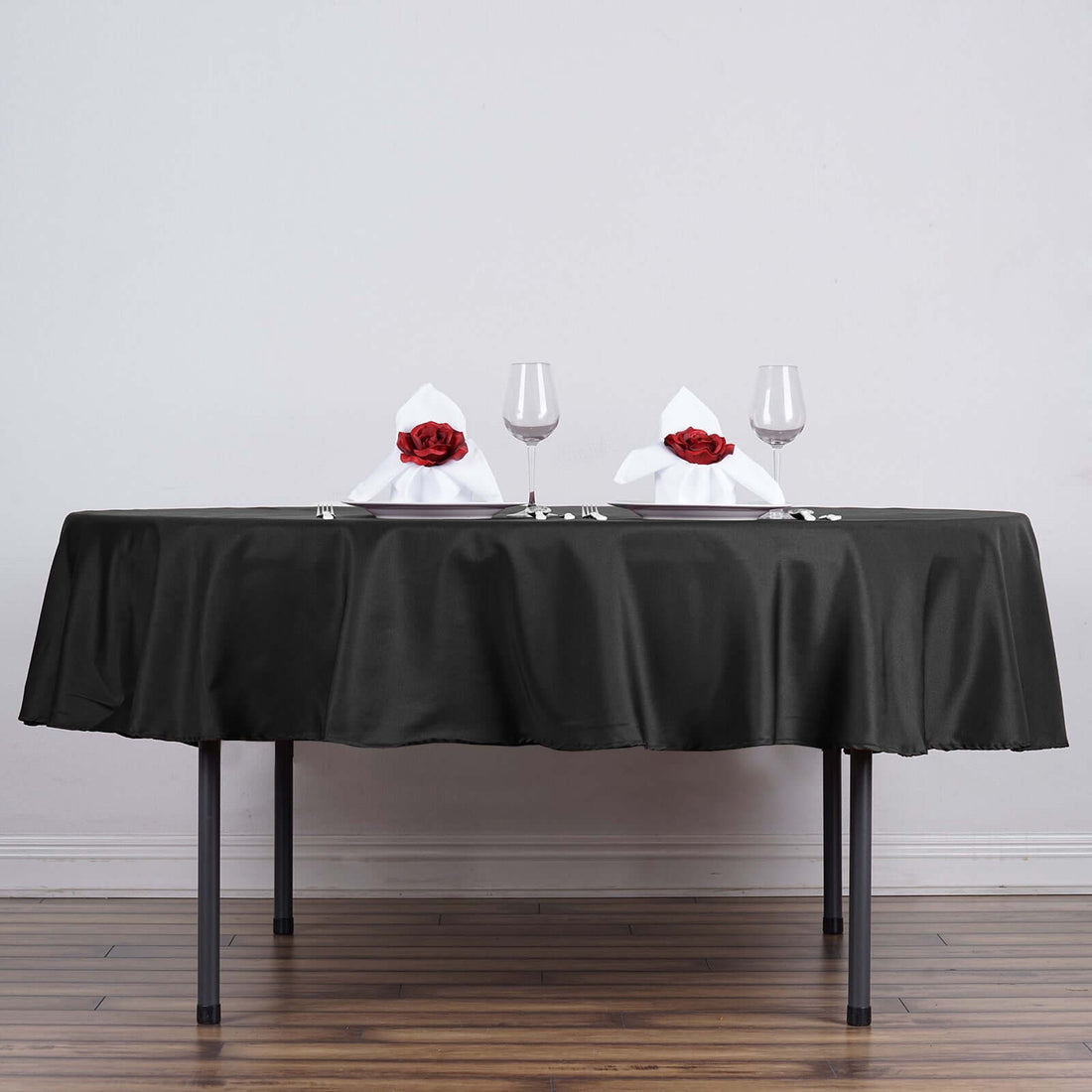 Elegant dining setup with black tablecloth, glasses, and rose-adorned napkins.