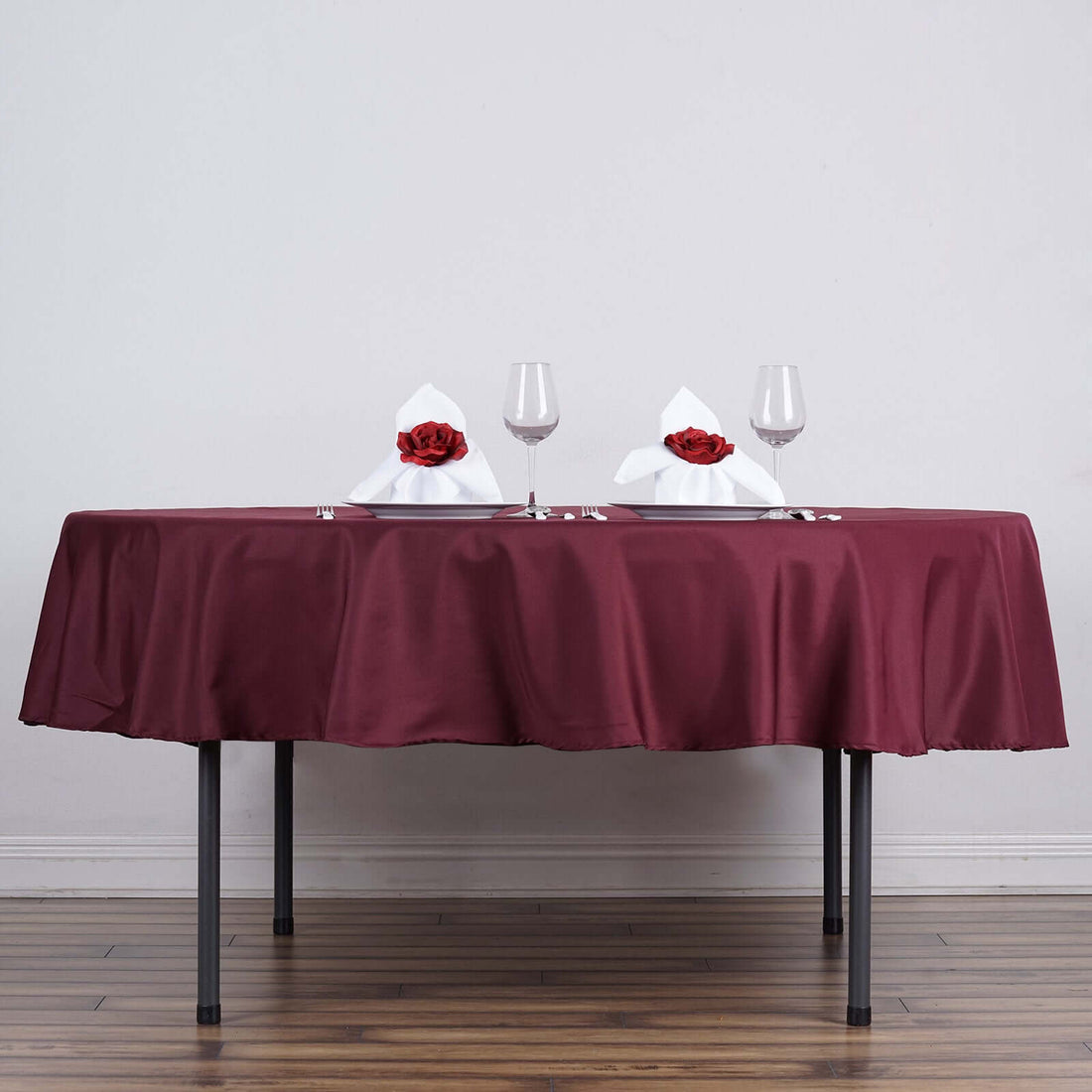 Elegant table setting with maroon tablecloth, white napkins, and rose accents.