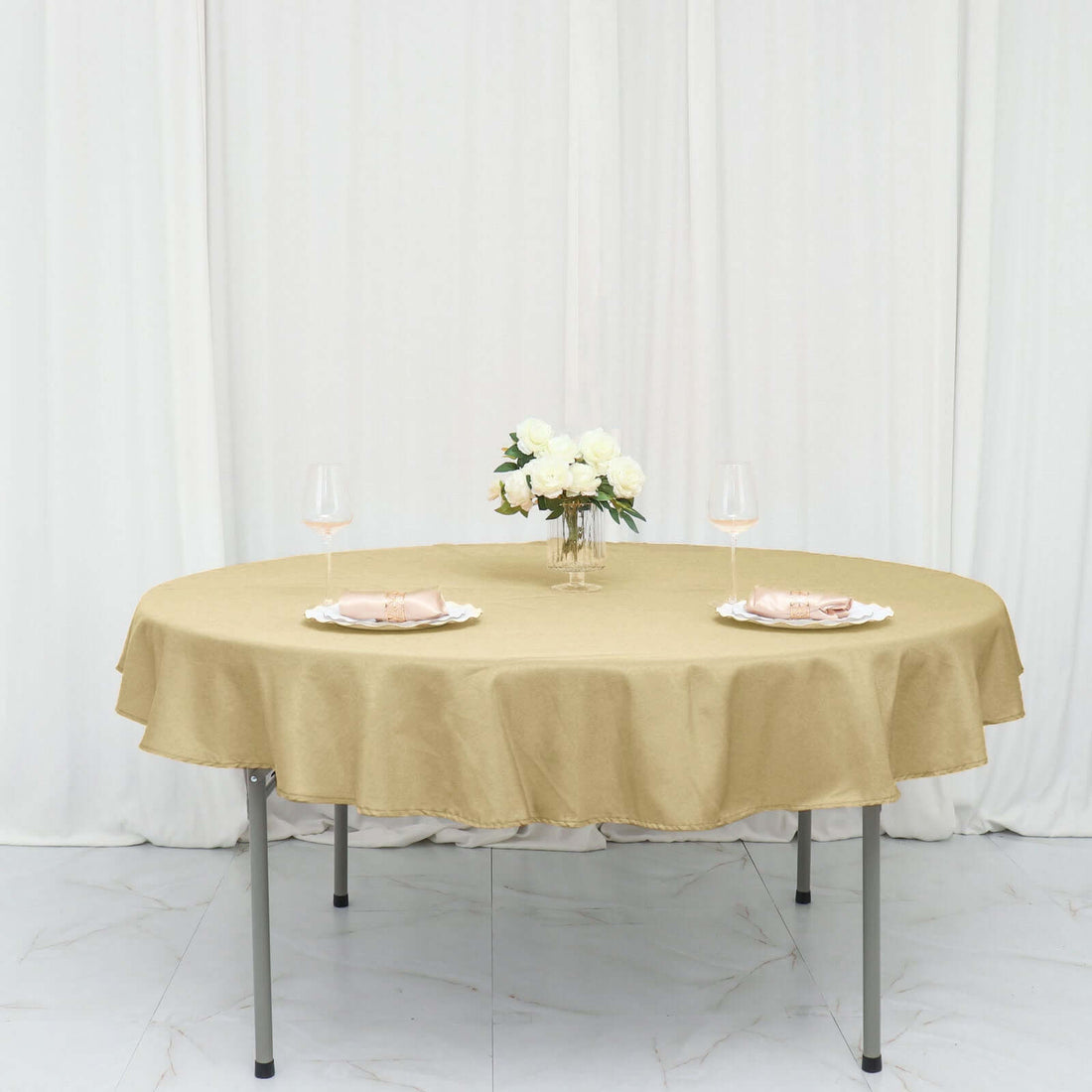 Round gold tablecloth draped over a table set for two with flowers and glasses.