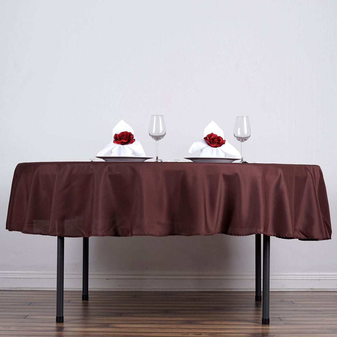 Elegant brown tablecloth set for a romantic dinner with wine glasses and rose-adorned napkins.