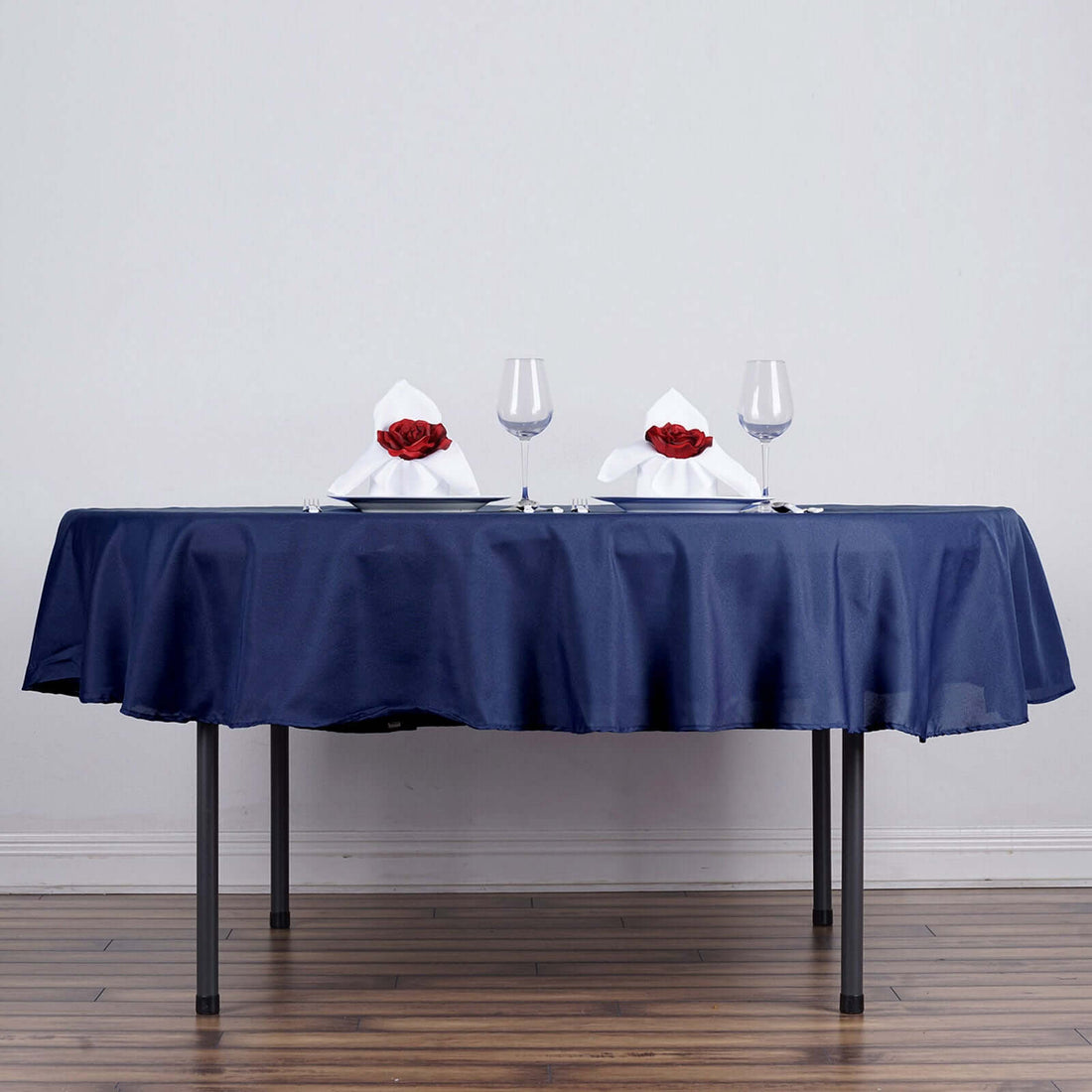 Elegant navy tablecloth set for a romantic dinner with glasses and rose-adorned napkins.