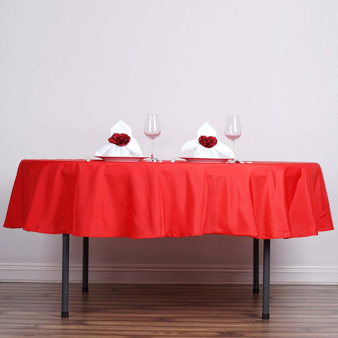 Elegant red table setting with wine glasses and flower-adorned napkins.
