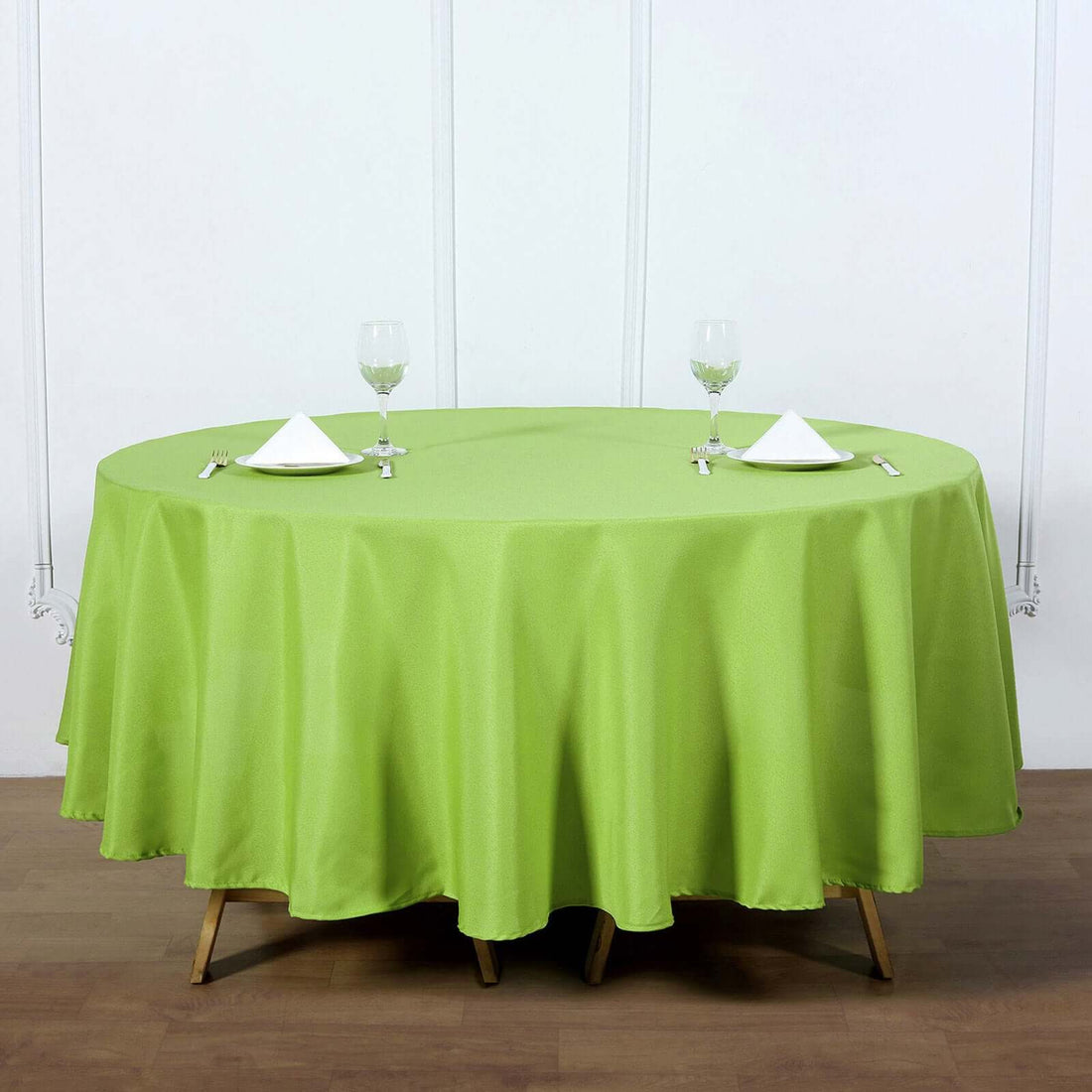 Green round tablecloth on a wooden table with plates and glasses.