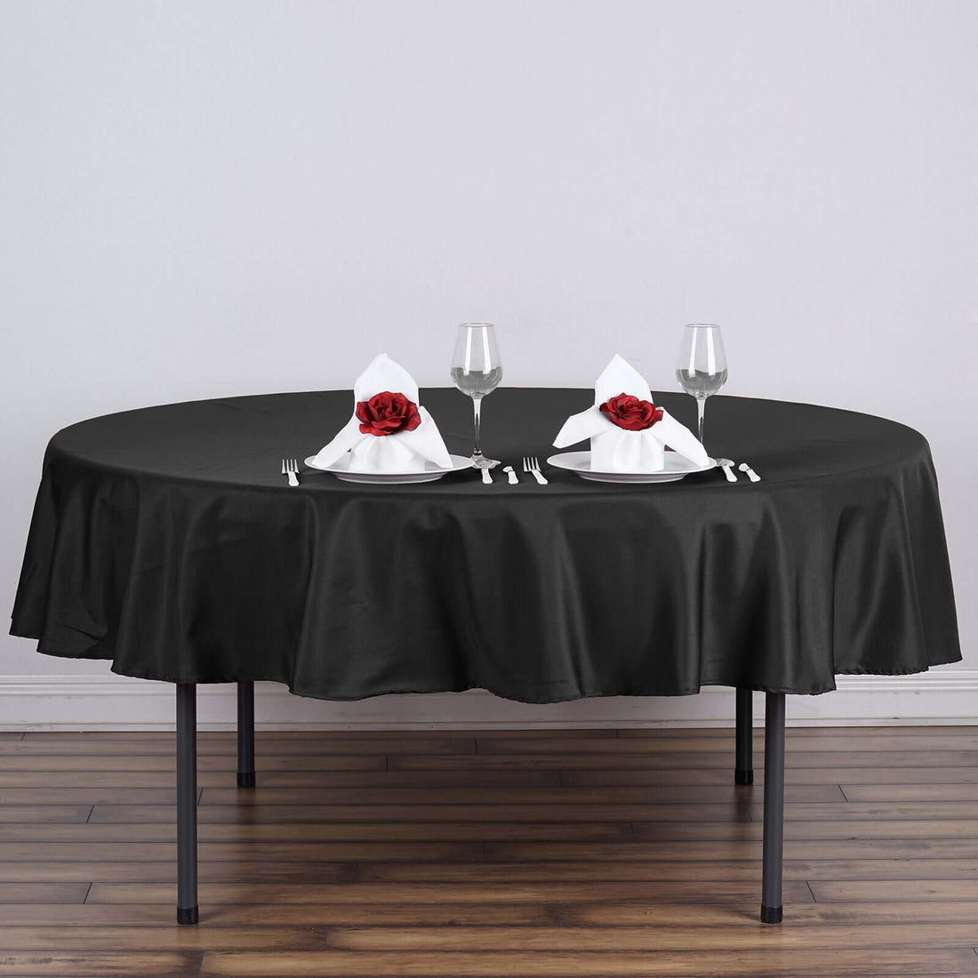 Elegant black tablecloth set for dining with rose-adorned napkins and glassware.