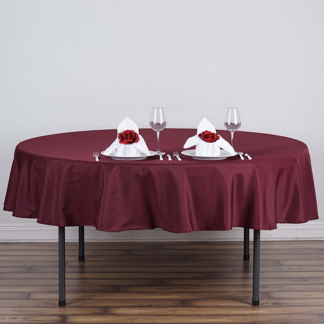 Round burgundy tablecloth with elegant napkin and rose centerpiece setup.