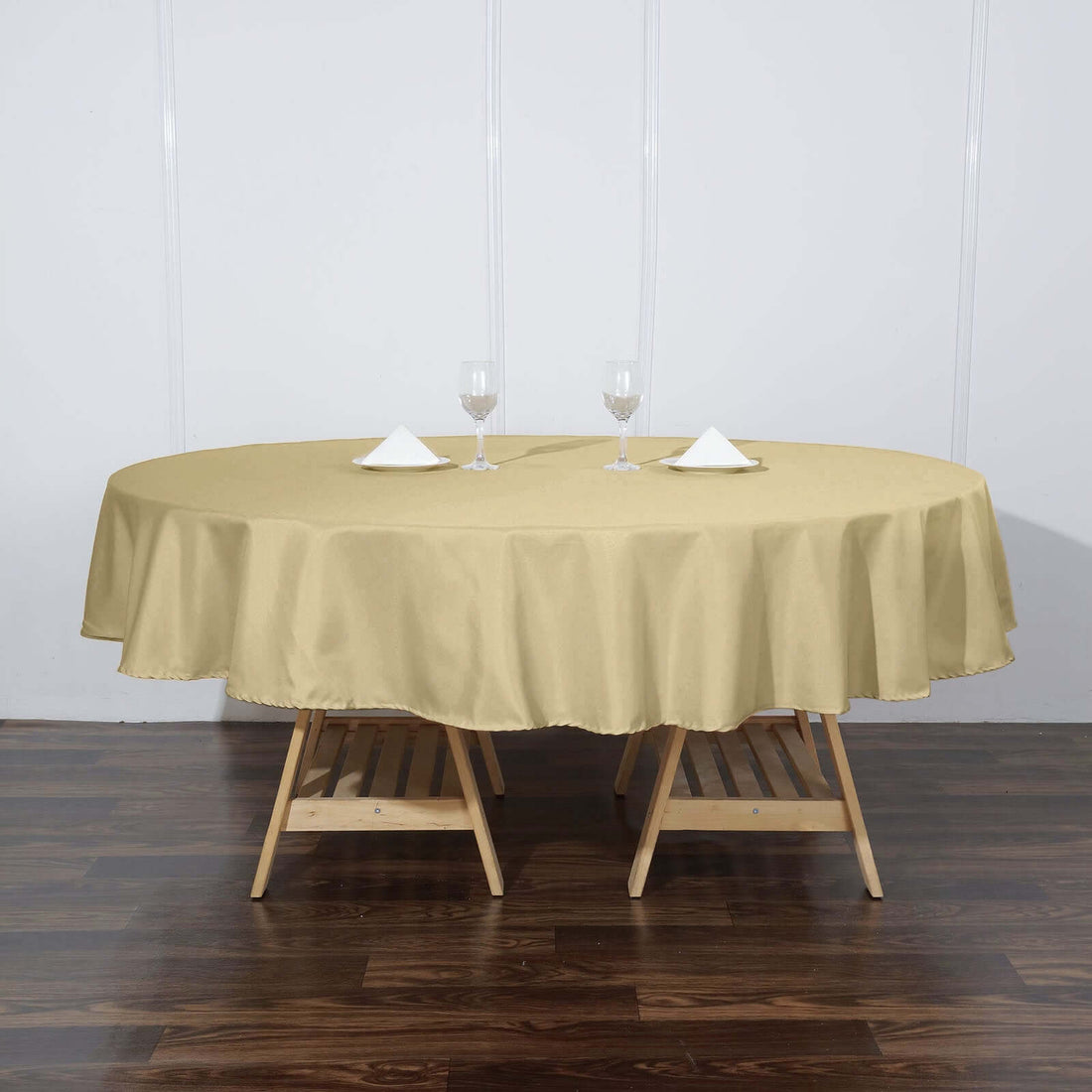 Round gold tablecloth draped over a wooden table with glasses and napkins.