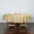 Round gold tablecloth draped over a wooden table with glasses and napkins.