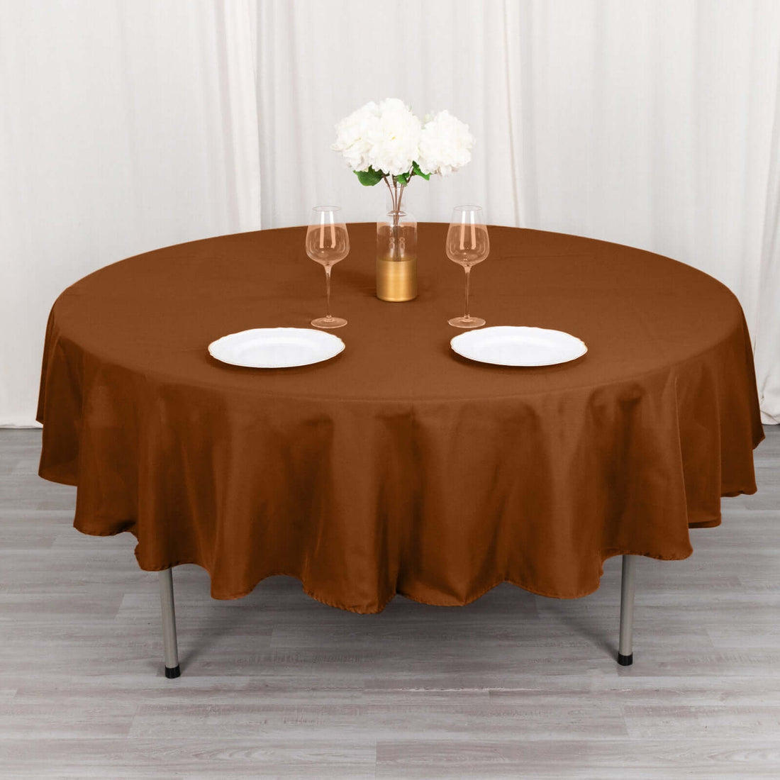 Round brown tablecloth on a dining table set with plates and glasses.