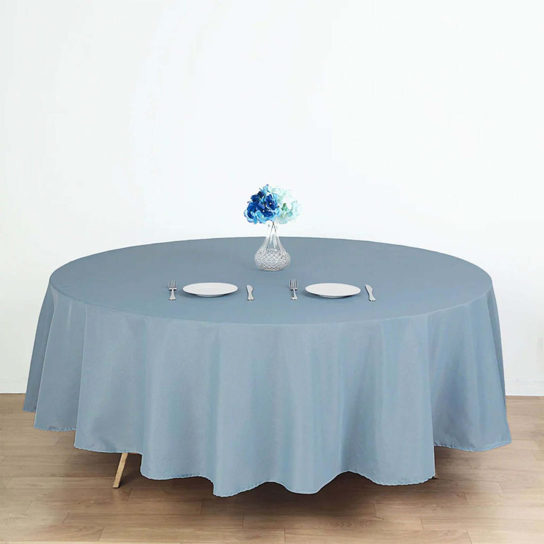 Round blue tablecloth draping a table with plates and a floral centerpiece.