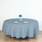 Round blue tablecloth draping a table with plates and a floral centerpiece.
