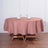 Round pink tablecloth draped over a wooden table set with glasses and napkins.