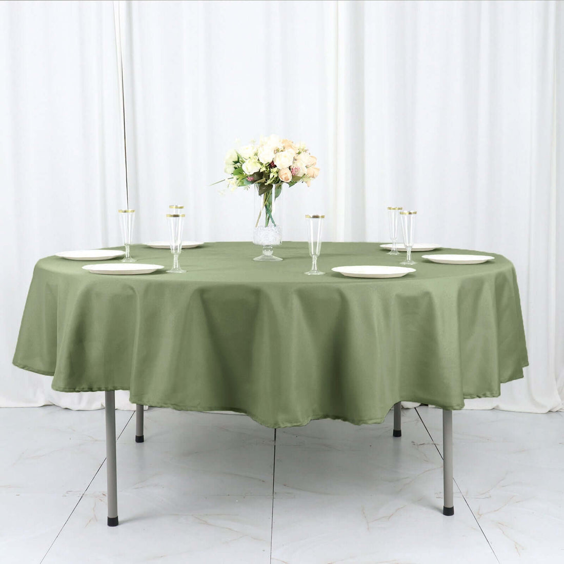 Olive green tablecloth on a round table set for dining with floral centerpiece.