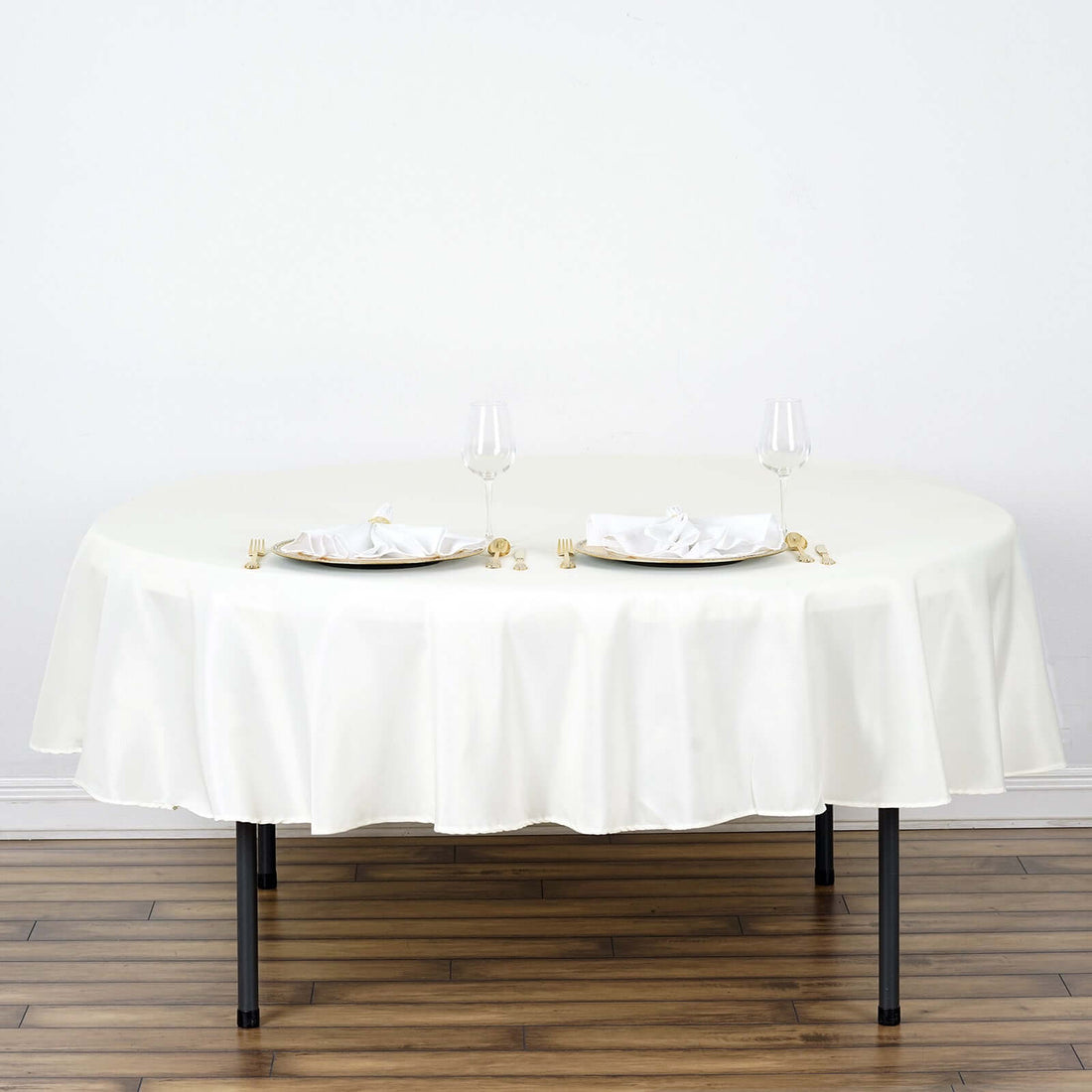 Round white tablecloth draped over a table with elegant dinnerware and glasses