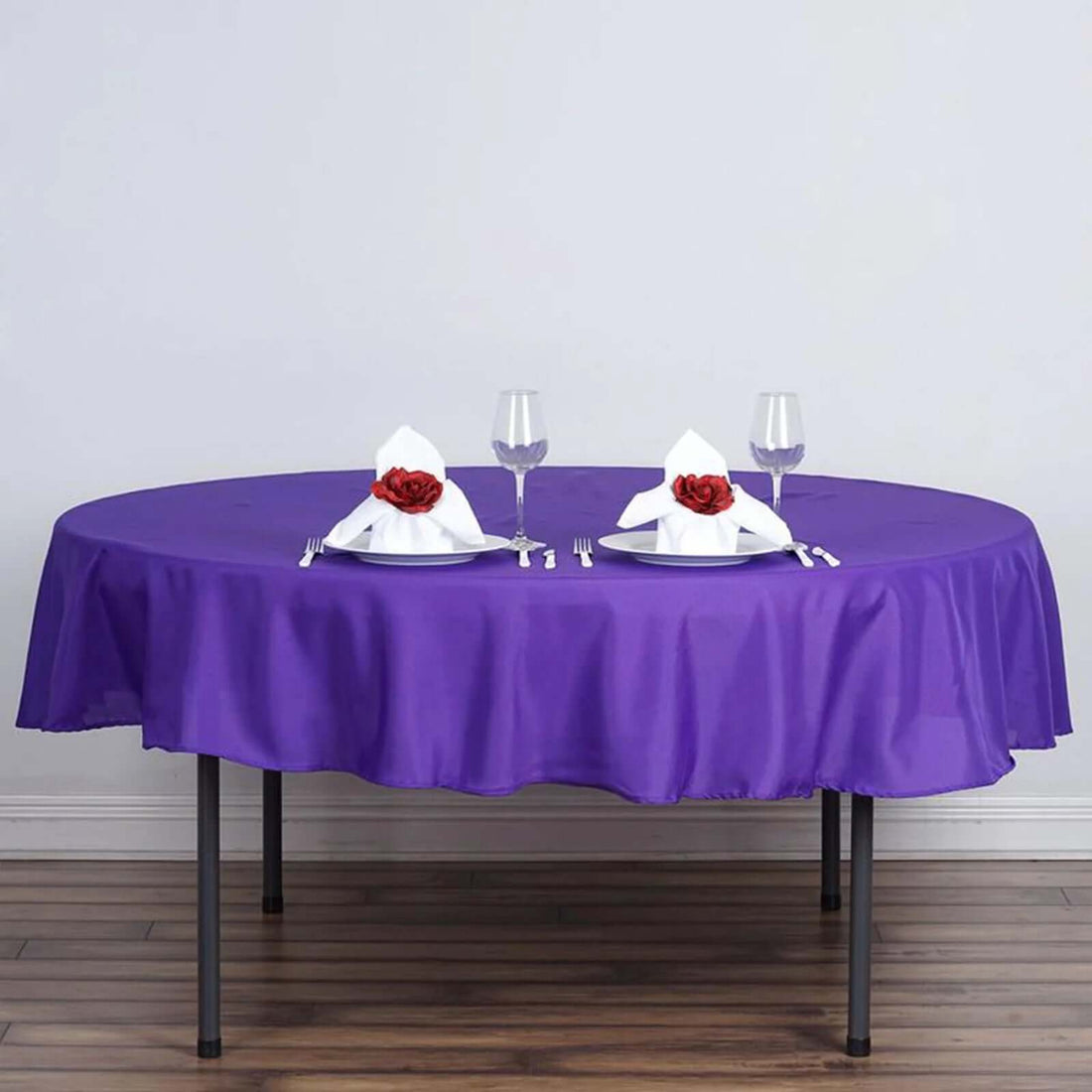Purple tablecloth draped over a round table set for dinner with decorative napkins.