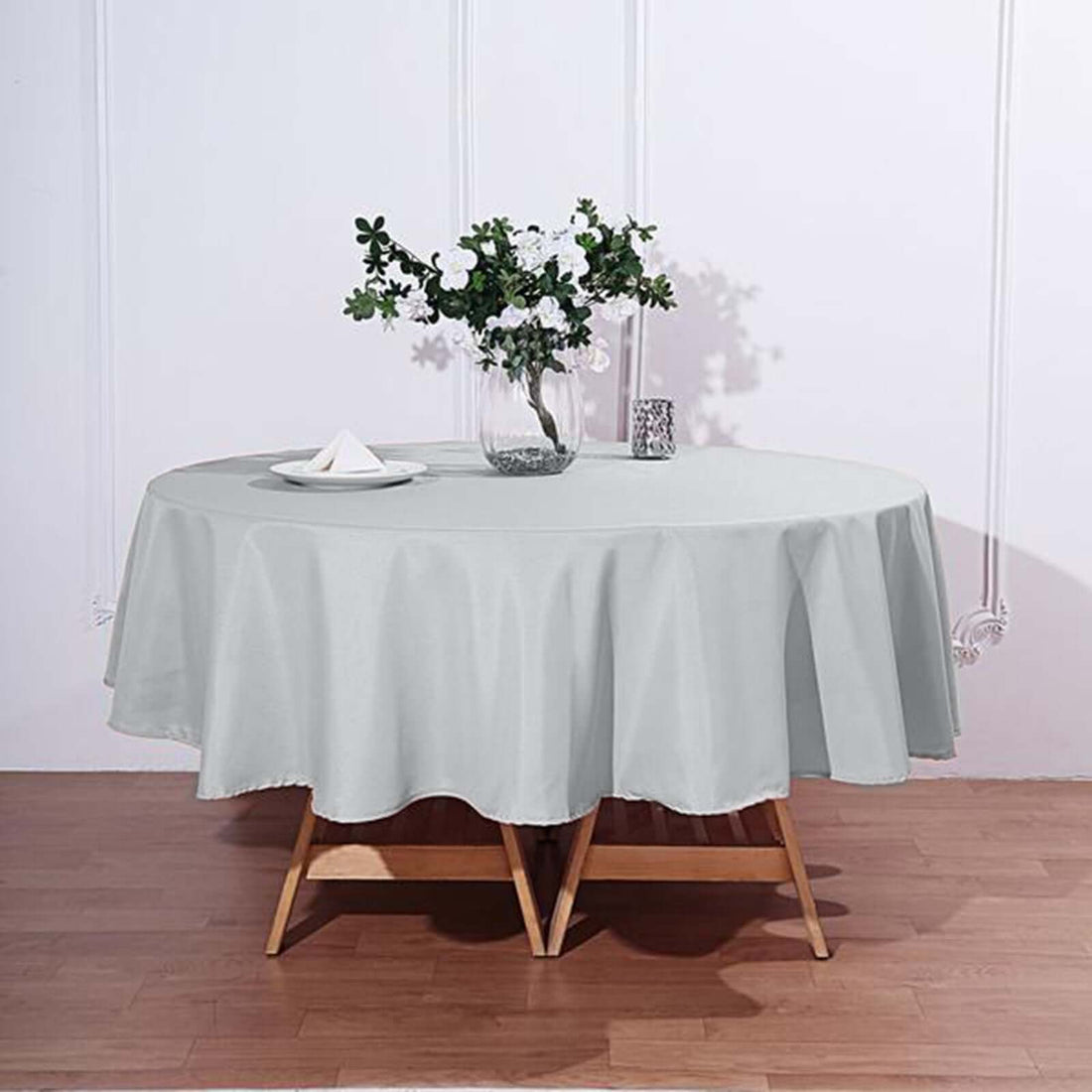 Round gray tablecloth draped over a wooden table with floral centerpiece.